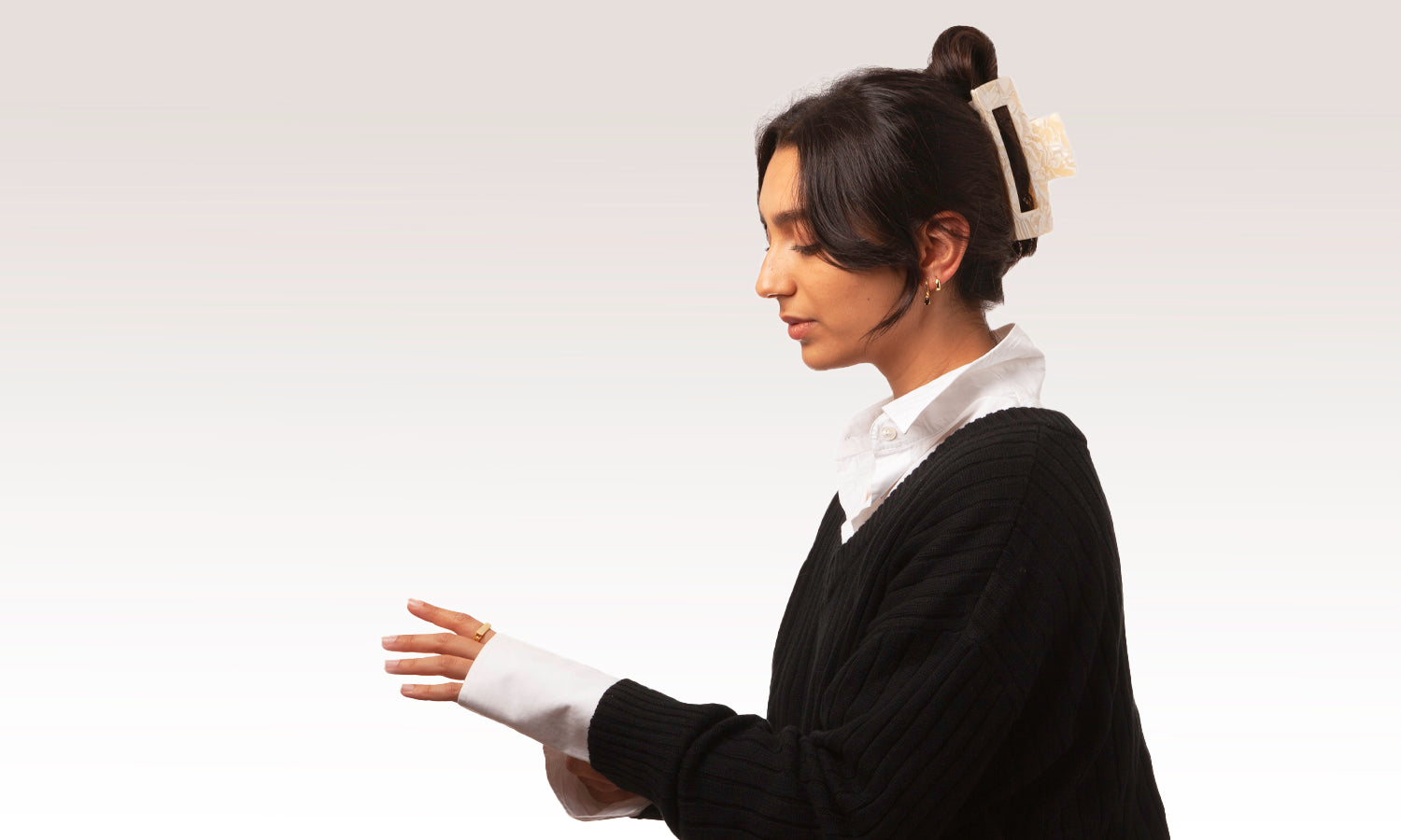 Brunette model wearing the Bondi Claw clip in white marble with gold earrings, chain signet ring and necklaces. She is wearing a white cotton shirt and black jumper.